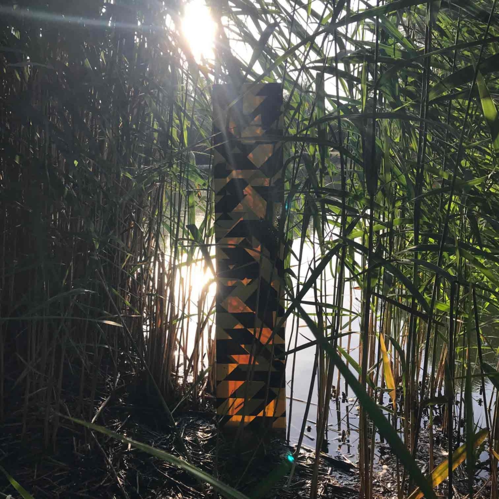 canvas covered in hazard tape in reeds next to a pond